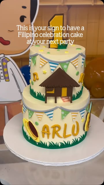 Two-tier Filipino-themed celebration cake with a nipa hut topper and the name Arlo